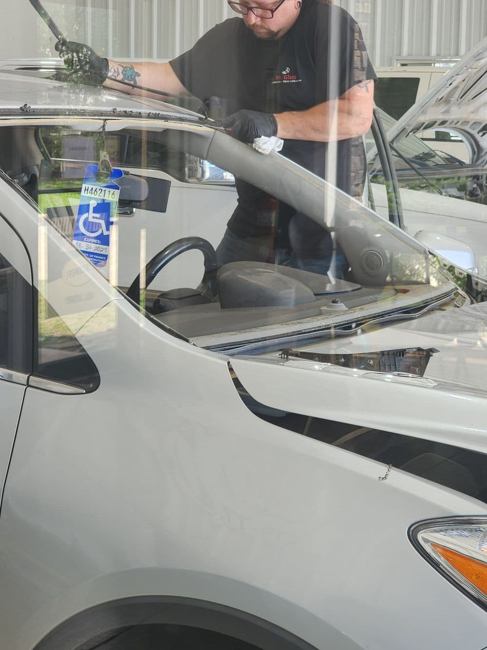 Auto technician replacing windshield of a vehicle in a garage setting.