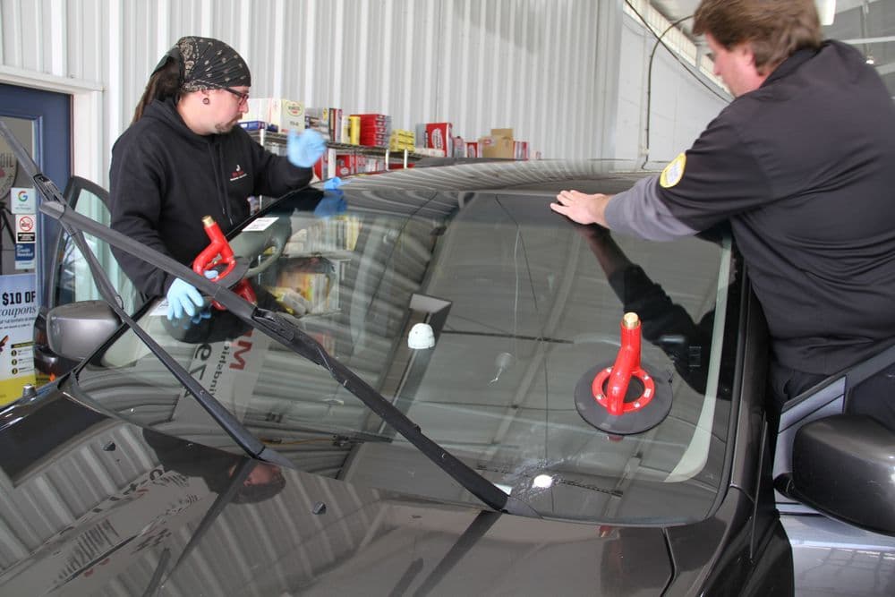Technicians replacing a vehicle windshield in an auto repair shop.