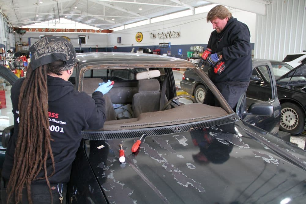 Technicians repairing a car windshield in an auto body shop with tools and equipment.