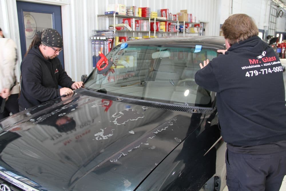 Technicians repairing a windshield at an auto glass service shop. Tools and equipment visible.