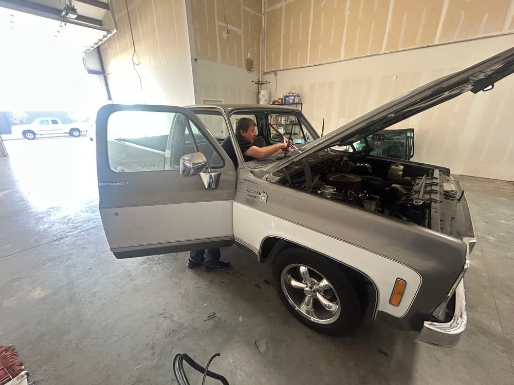 Mechanic working on classic truck engine in spacious garage with tools and equipment.