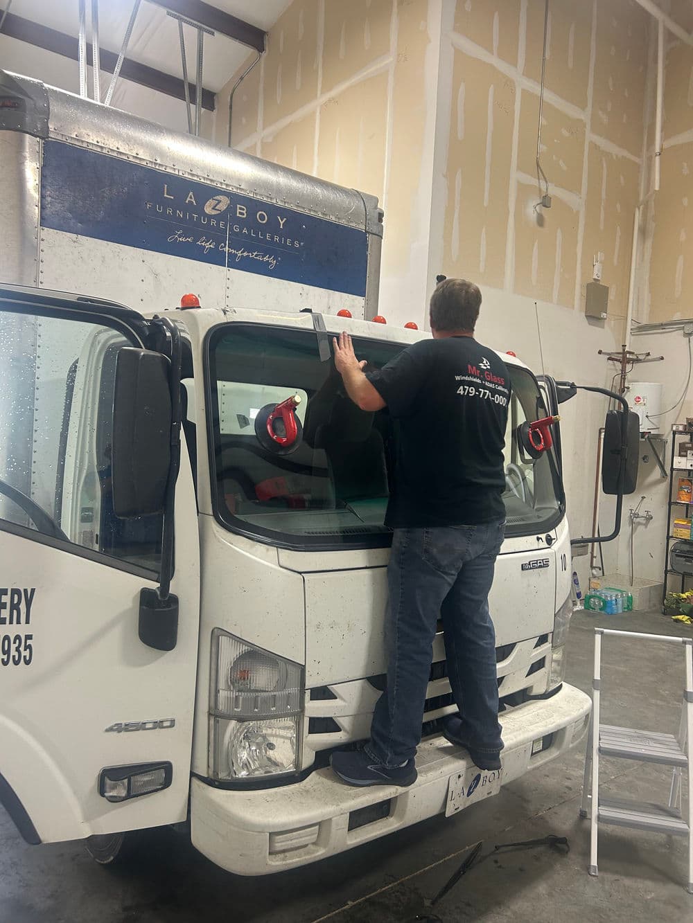 Worker installing a windshield on a delivery truck in a garage setting.