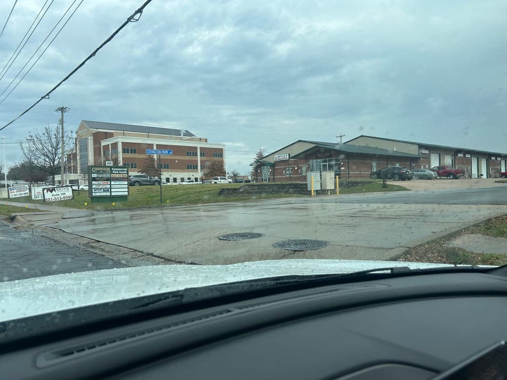View of commercial buildings along a wet street, showcasing signage and cloudy skies.