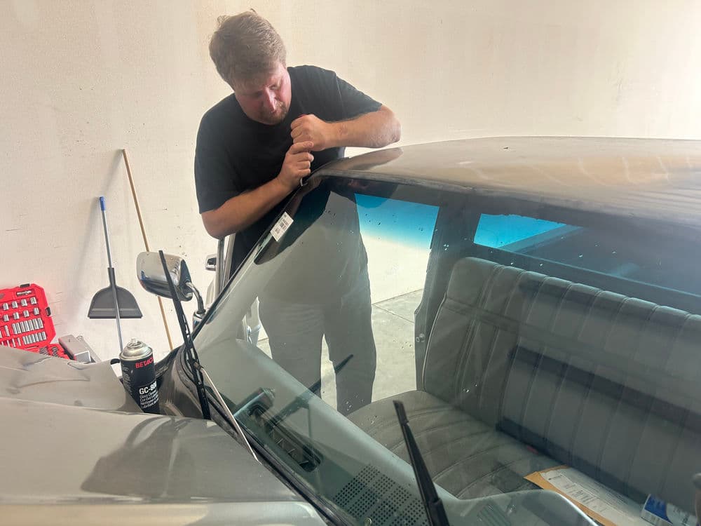 Man repairing a car windshield in a garage, focusing on detailed work with tools.