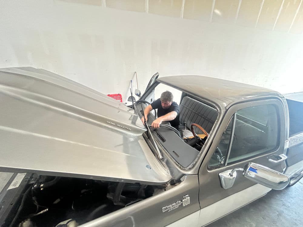 Mechanic working on an open hood of a classic pickup truck in a garage setting.